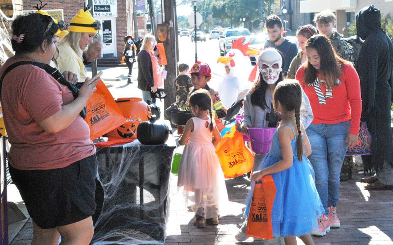 Halloween on the Square attendees, including two princesses and a fireman, can be seen approaching the Light and Champion staff as they disperse candy.
