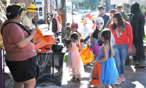 Halloween on the Square attendees, including two princesses and a fireman, can be seen approaching the Light and Champion staff as they disperse candy. 